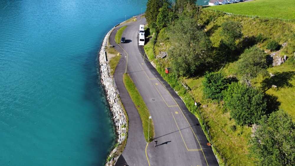 Numbered coach bays marked in yellow along the shore road above the fjord, with a coach parked at the far end and the water running the length of the frame
