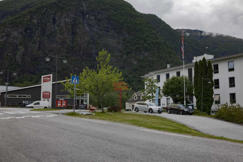 The centre of Skjolden village on an overcast day: the supermarket, the hotel, a pedestrian crossing and the road, with the mountain wall rising directly behind