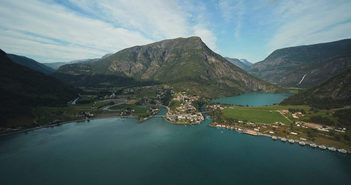 Aerial view over the head of the fjord to Skjolden: the village on the flat ground between the fjord and the lake behind it, farmland along both shores and a waterfall coming down the mountainside on the right
