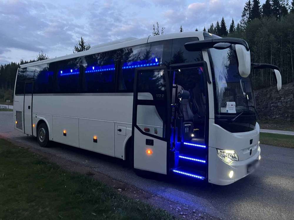 A white midi coach at dusk with its door open and courtesy lighting glowing along the sills