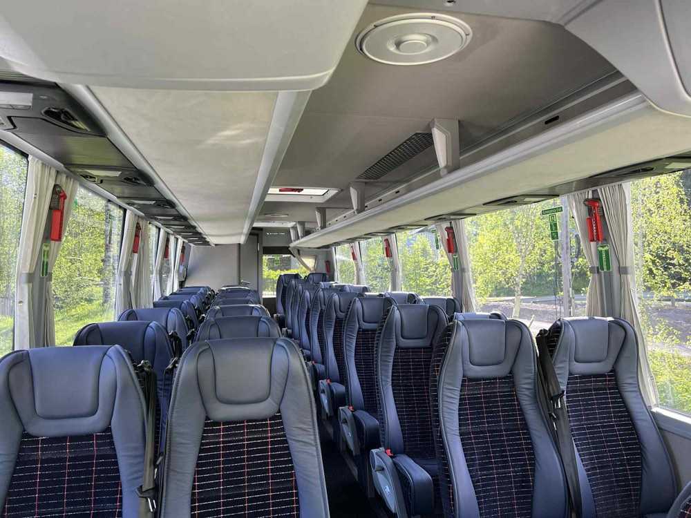 Interior of a midi coach looking down the aisle past rows of high-back seats with seatbelts