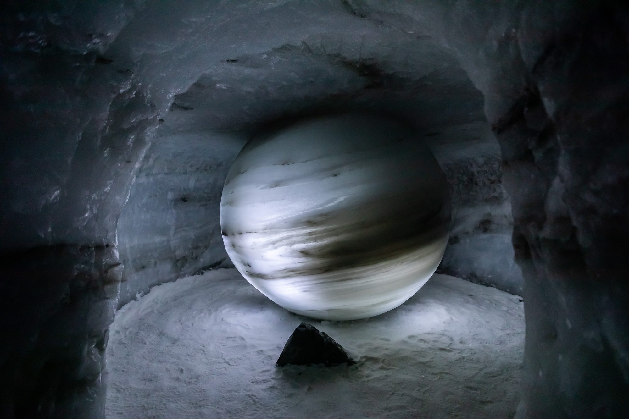 A great sphere of layered glacier ice resting in a chamber of the ice tunnel, the walls around it banded grey and white