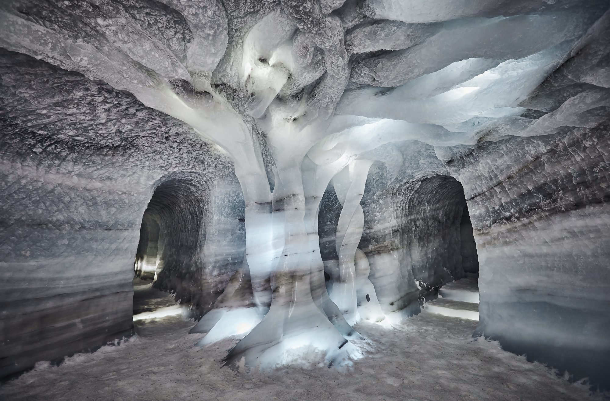 A tree carved from the glacier ice deep inside the ice tunnel, lit from within, with tunnel openings on either side of it