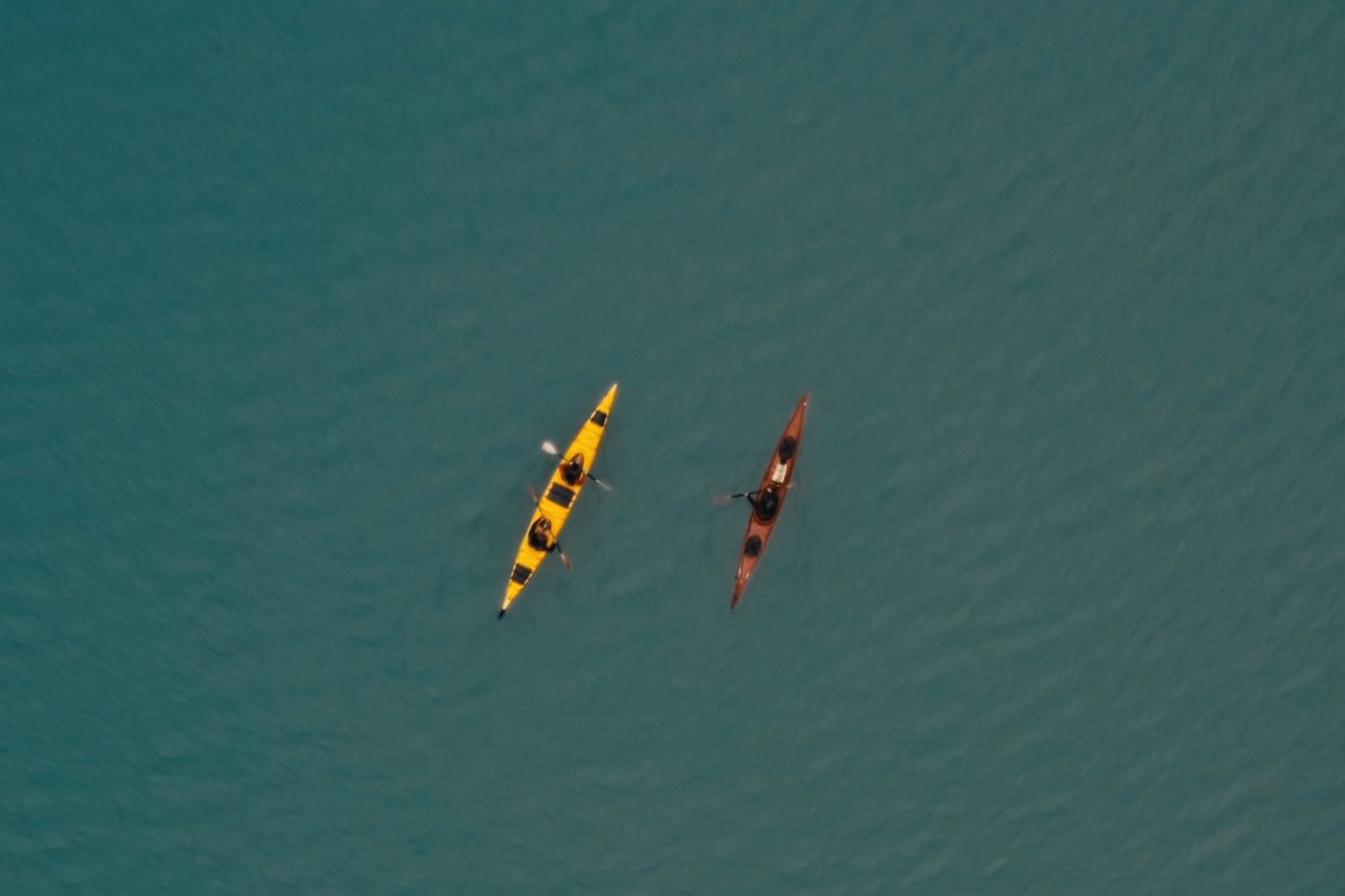 Two sea kayaks seen from directly above on still teal water, a yellow double and a red single