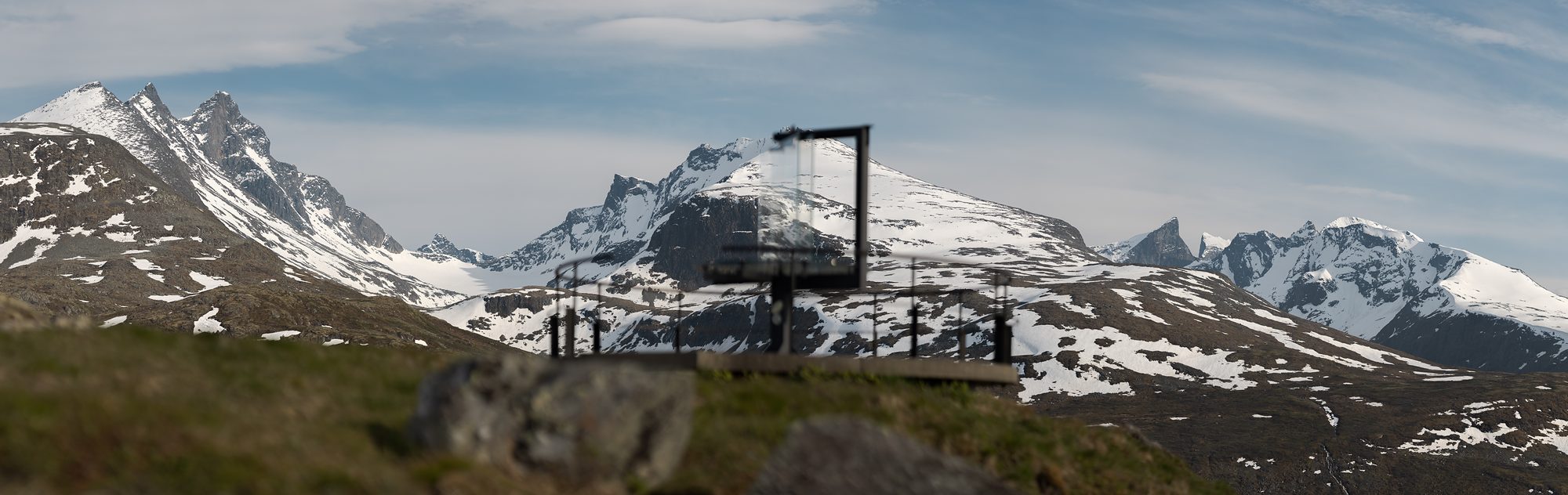 Panorama of the jagged, snow-covered Hurrungane with the glass panorama marker at Oscarshaug small in the middle distance