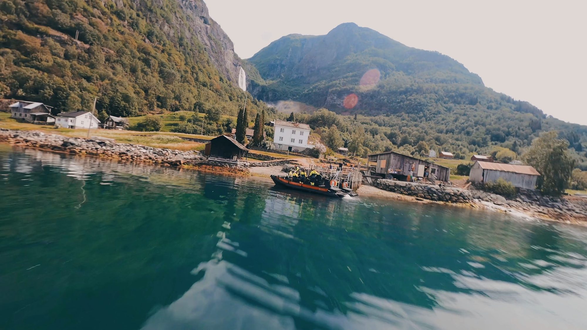 A RIB coming in to the landing at Feigum, low over green water, with the farm on the shore and the waterfall high on the mountain behind