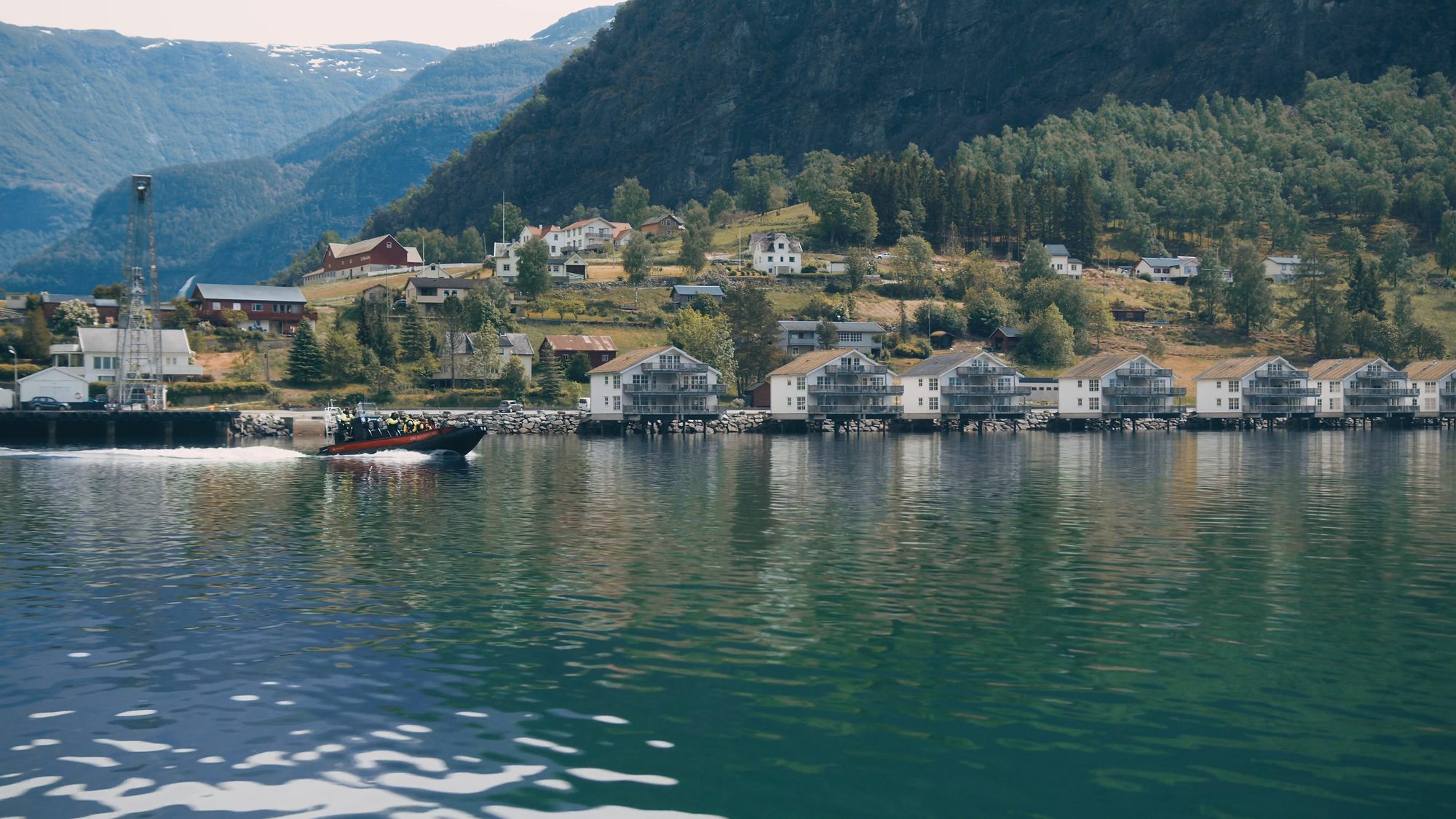 A RIB heading out from Skjolden, the row of houses on the shore and the village on the slope behind it