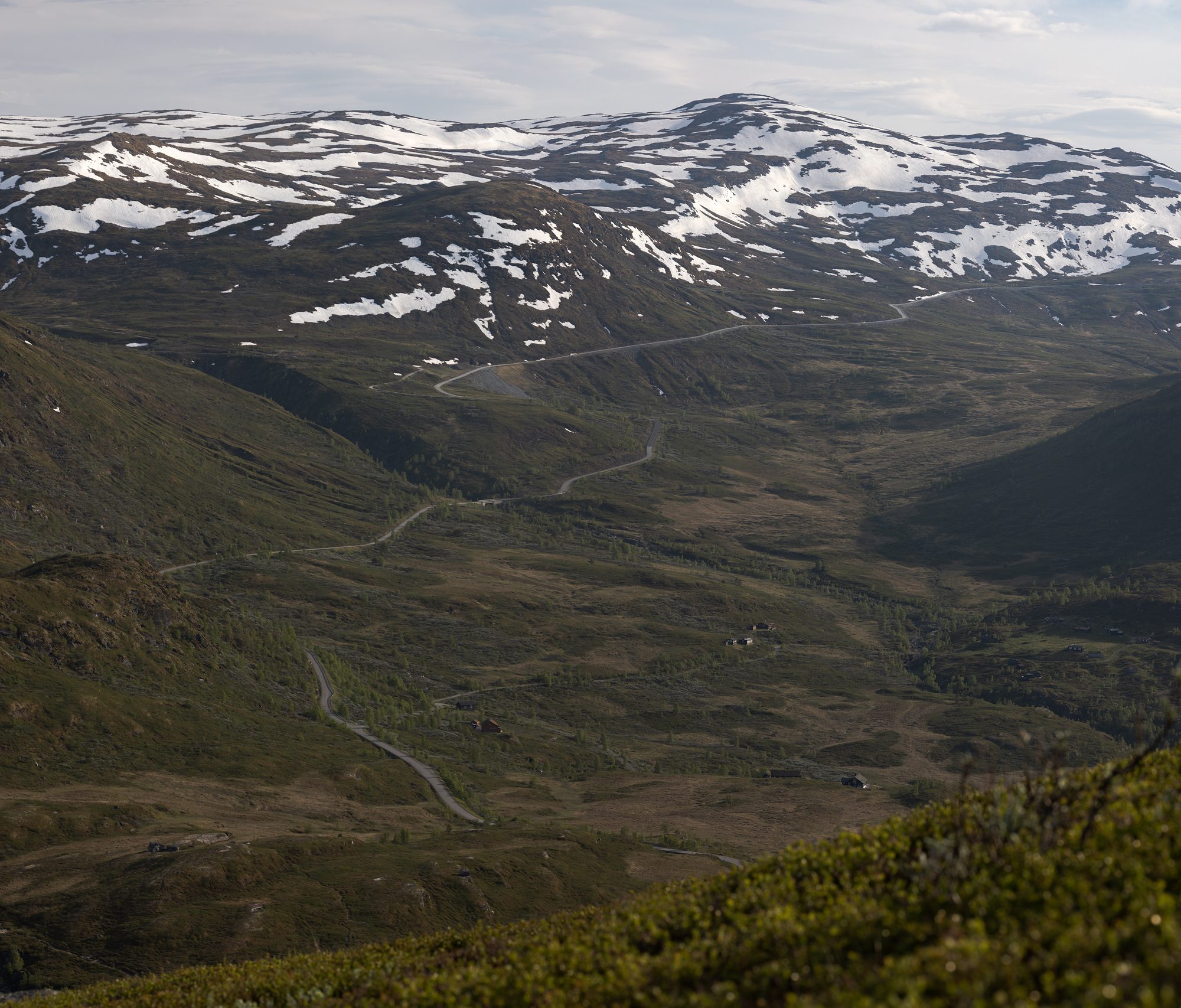 A wide mountain valley with a road winding up through it towards snow-patched summits
