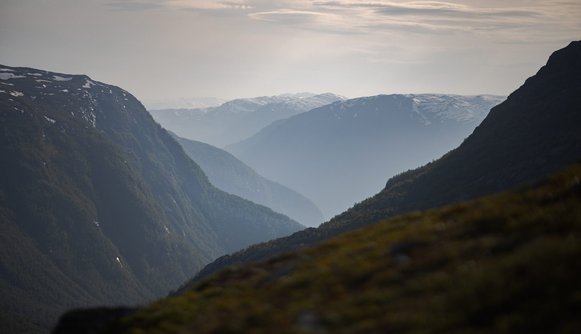 Blue mountain ridges receding down a deep valley towards the fjord in hazy afternoon light