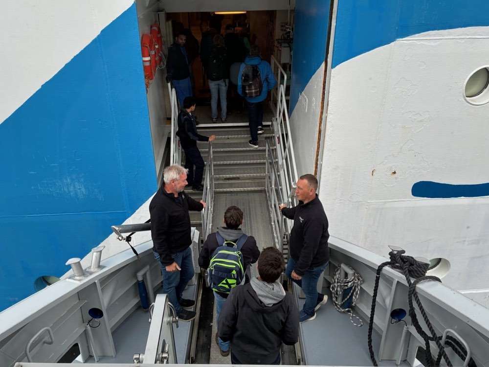 Passengers walking up a metal gangway from a tender boat into a ship's side door